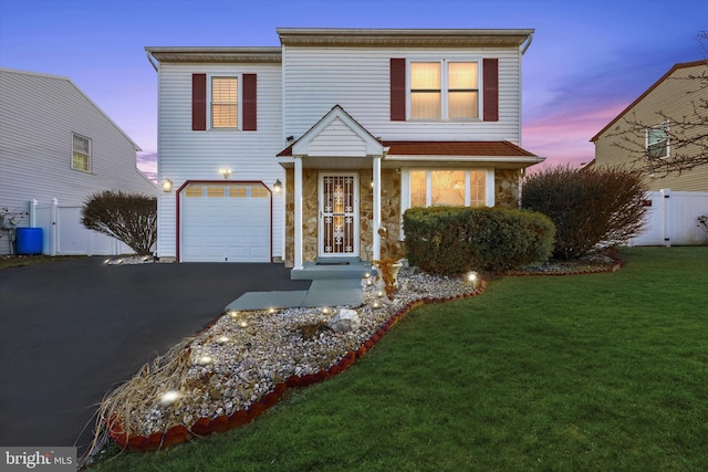 traditional-style home featuring a garage, a front lawn, fence, and aphalt driveway