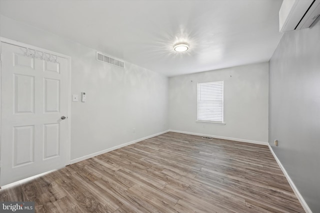 unfurnished room featuring a wall unit AC, light wood finished floors, baseboards, and visible vents