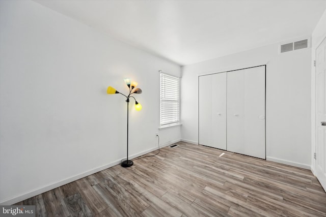 unfurnished bedroom featuring light wood-type flooring, a closet, visible vents, and baseboards