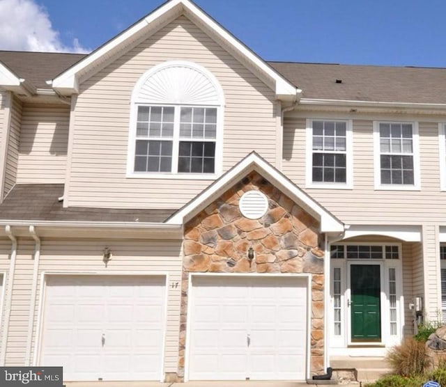 view of property featuring stone siding, roof with shingles, and an attached garage