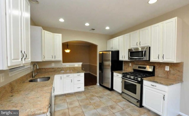 kitchen featuring arched walkways, decorative light fixtures, appliances with stainless steel finishes, white cabinets, and a sink