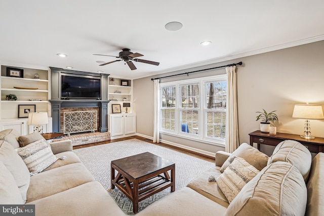 living room featuring a ceiling fan, wood finished floors, crown molding, a brick fireplace, and recessed lighting