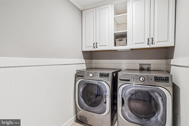 clothes washing area with a wainscoted wall, washing machine and clothes dryer, and cabinet space