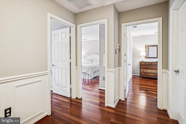 corridor with visible vents, dark wood-type flooring, and wainscoting