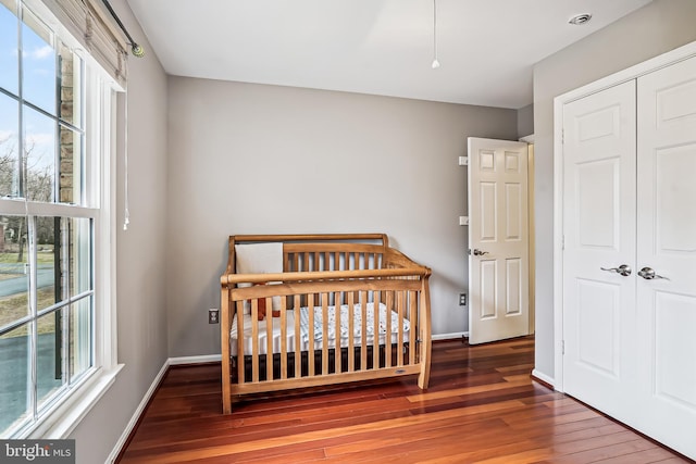 bedroom with hardwood / wood-style floors, a nursery area, baseboards, and a closet