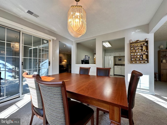 dining area featuring carpet, visible vents, a notable chandelier, and a textured ceiling