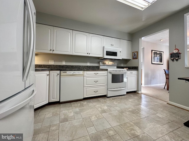 kitchen featuring white appliances, white cabinetry, stone finish floor, and baseboards