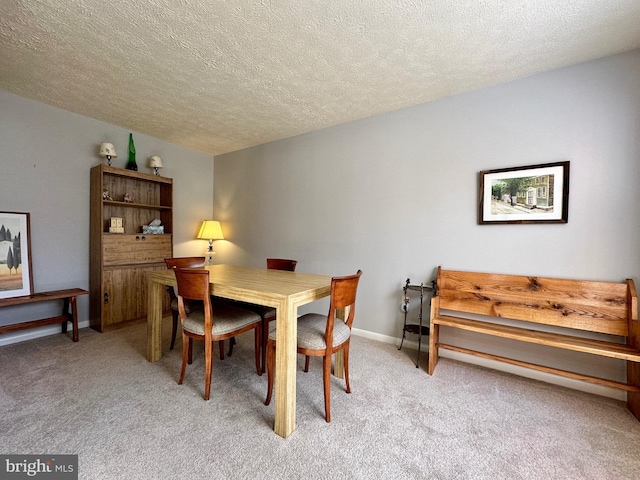 dining space featuring a textured ceiling, baseboards, and light colored carpet