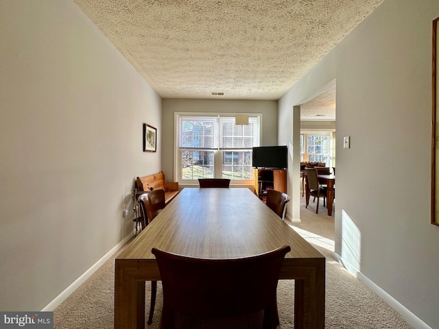 carpeted dining space with a textured ceiling, visible vents, and baseboards