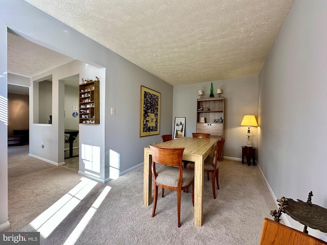 dining area with baseboards, a textured ceiling, and light colored carpet