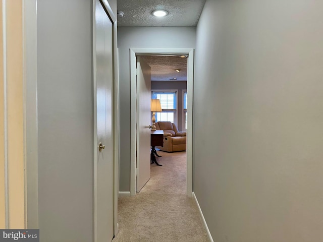 corridor featuring light carpet, a textured ceiling, and baseboards