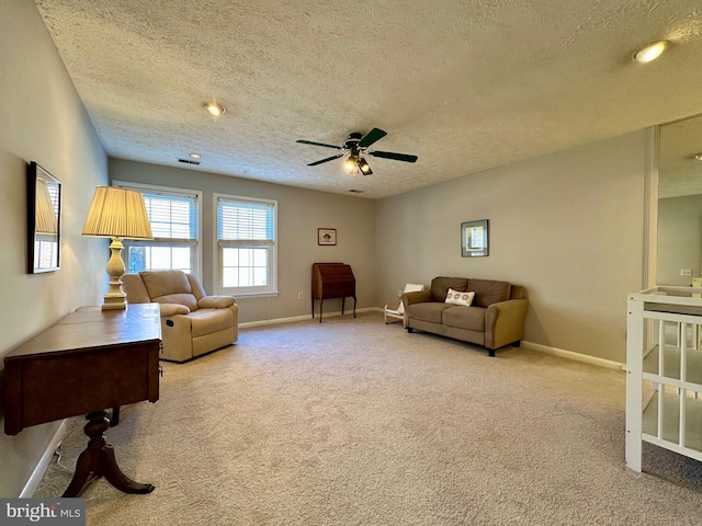 living area with light carpet, a textured ceiling, a ceiling fan, and baseboards