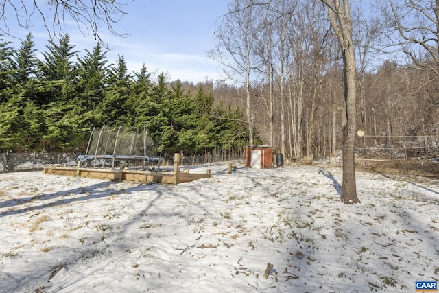 yard layered in snow featuring a trampoline, fence, and a wooded view