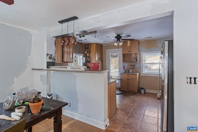 kitchen with a peninsula, freestanding refrigerator, open shelves, brown cabinetry, and decorative light fixtures