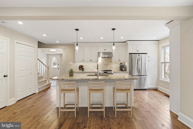 kitchen featuring freestanding refrigerator, white cabinetry, a sink, and an island with sink