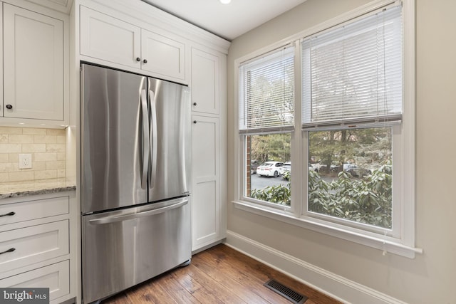 kitchen with light stone counters, visible vents, white cabinets, backsplash, and freestanding refrigerator