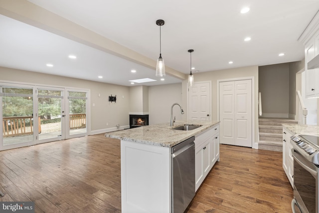 kitchen with light stone counters, stainless steel appliances, a kitchen island with sink, white cabinetry, and a sink