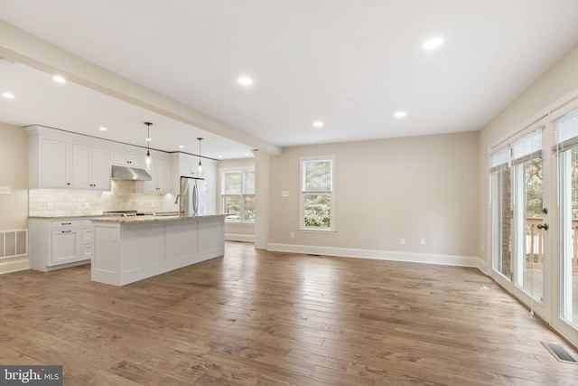 kitchen with visible vents, an island with sink, open floor plan, freestanding refrigerator, and white cabinetry