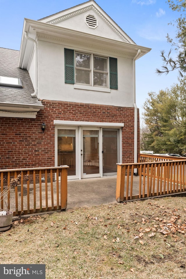 back of property featuring brick siding, a wooden deck, and stucco siding