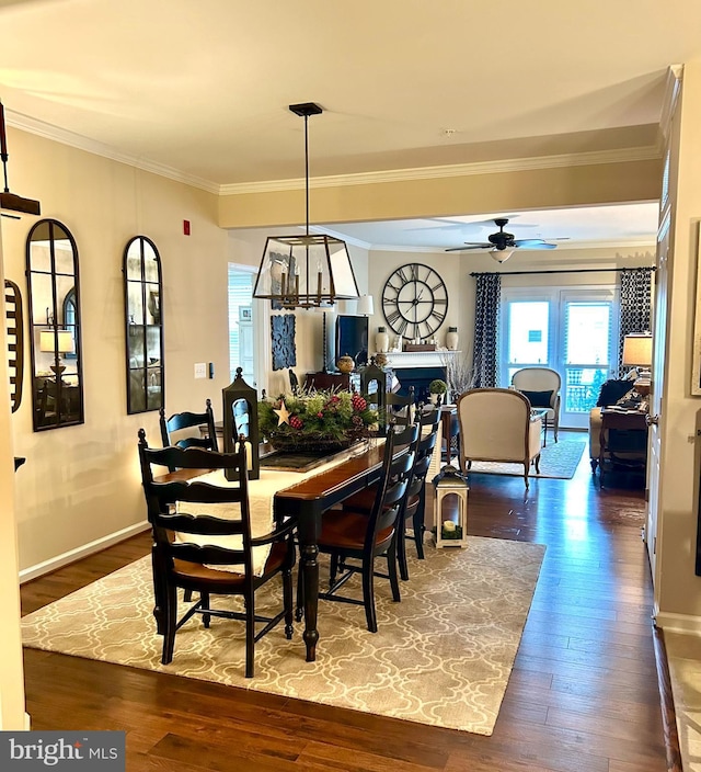 dining space with ceiling fan, a fireplace, baseboards, dark wood finished floors, and crown molding