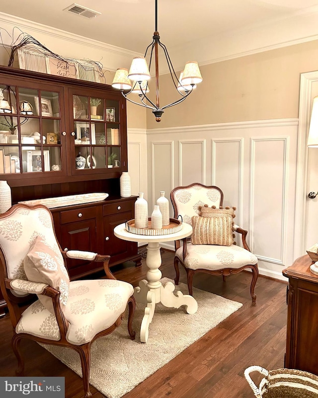 living area featuring a wainscoted wall, visible vents, ornamental molding, dark wood-type flooring, and a chandelier