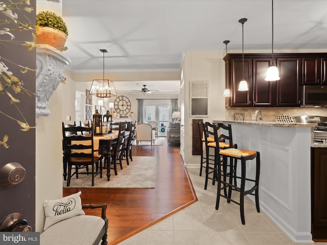 kitchen with stainless steel microwave, a breakfast bar, open floor plan, hanging light fixtures, and light stone countertops