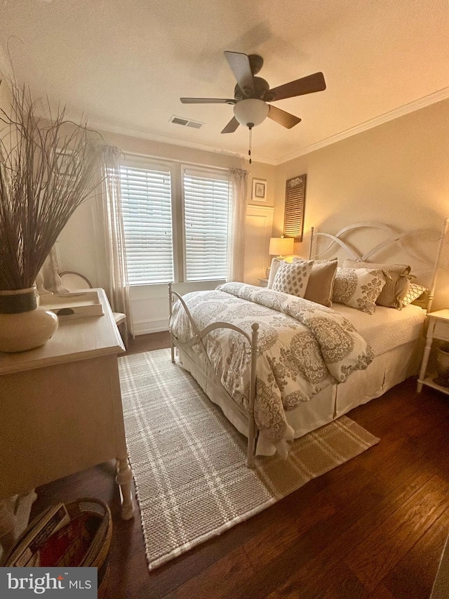 bedroom featuring a ceiling fan, visible vents, dark wood-style flooring, and ornamental molding