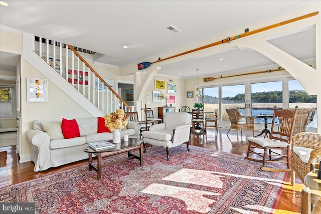 living area featuring arched walkways, crown molding, visible vents, a water view, and stairway