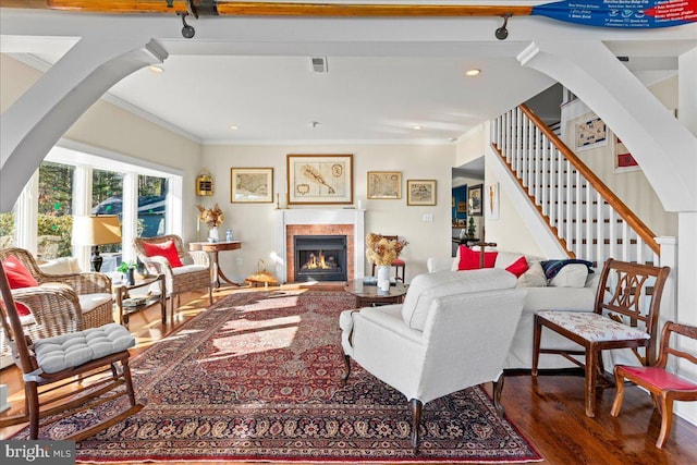 living room featuring visible vents, stairs, a lit fireplace, dark wood-style floors, and crown molding