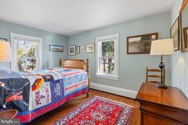 bedroom with a baseboard heating unit, baseboards, and wood finished floors