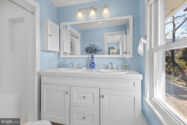 full bath featuring tiled shower, a sink, and double vanity