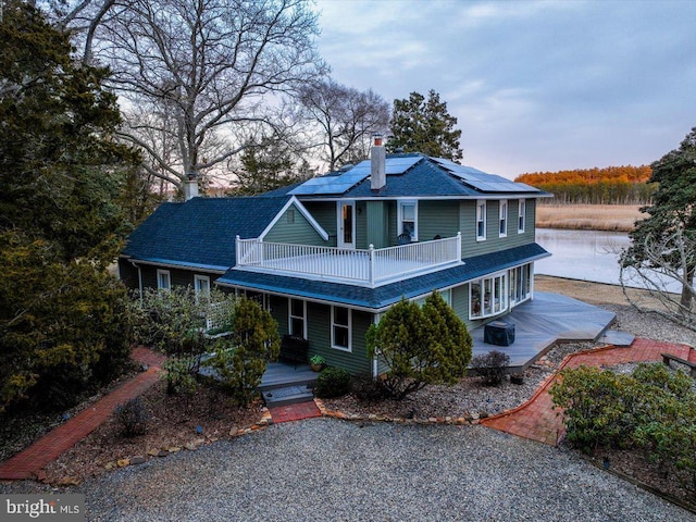 view of front of house featuring a balcony, a water view, a chimney, and solar panels