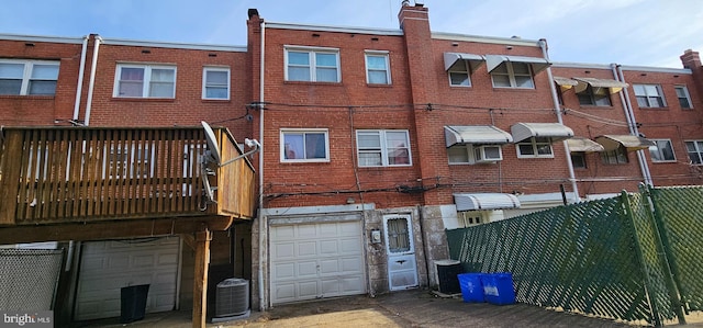 rear view of property with central AC unit, a garage, brick siding, fence, and driveway