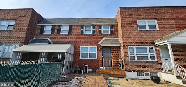 view of property featuring brick siding, fence, and roof with shingles