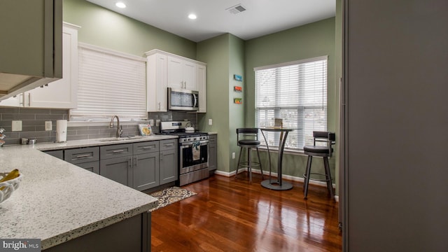 kitchen with stainless steel appliances, a sink, visible vents, backsplash, and dark wood finished floors