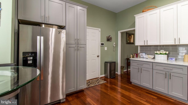 kitchen with stainless steel fridge with ice dispenser, dark wood-style floors, light stone countertops, gray cabinets, and backsplash