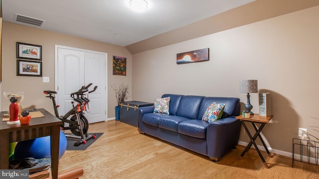 workout area featuring baseboards, visible vents, vaulted ceiling, and light wood finished floors