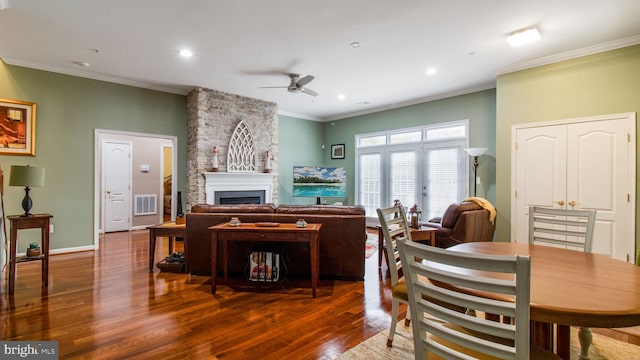 living area featuring a fireplace, a ceiling fan, visible vents, dark wood-style floors, and crown molding