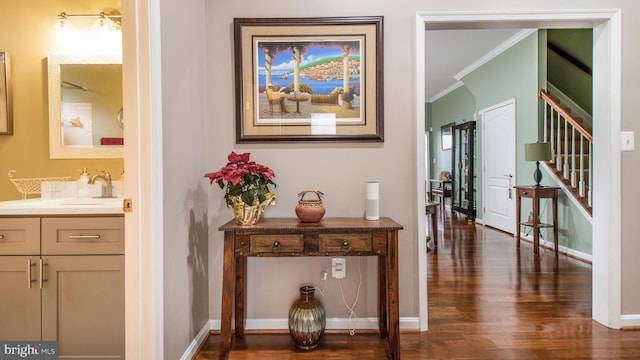 hall featuring a sink, baseboards, stairs, ornamental molding, and dark wood finished floors