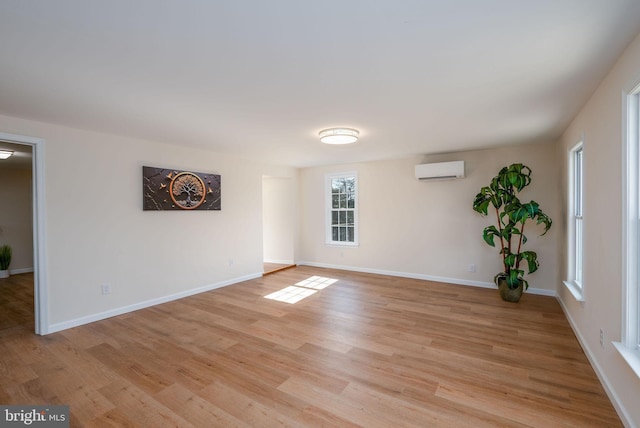 empty room with light wood-type flooring, baseboards, and a wall mounted AC