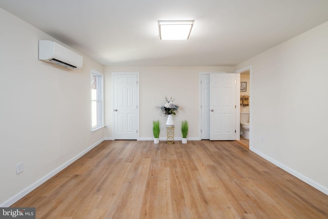 unfurnished room with light wood-style floors, baseboards, and an AC wall unit