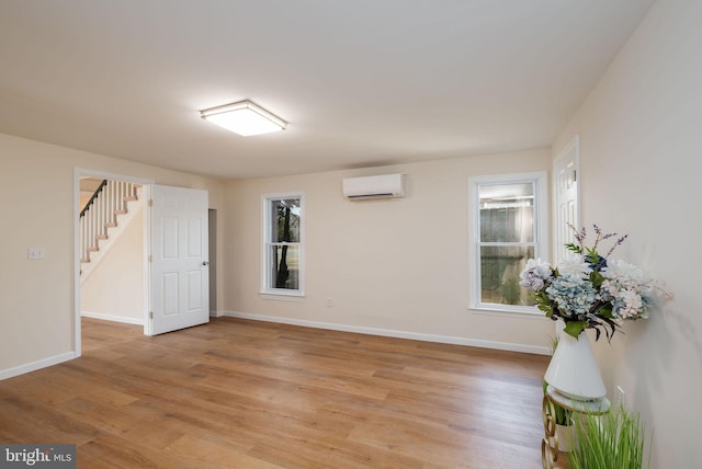 spare room with an AC wall unit, stairway, a wealth of natural light, and light wood-style floors