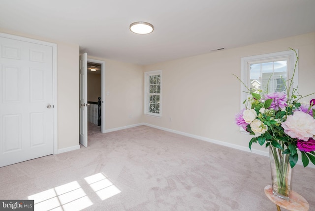 spare room featuring light colored carpet, visible vents, and baseboards