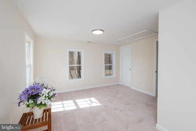 empty room featuring light carpet, attic access, and baseboards