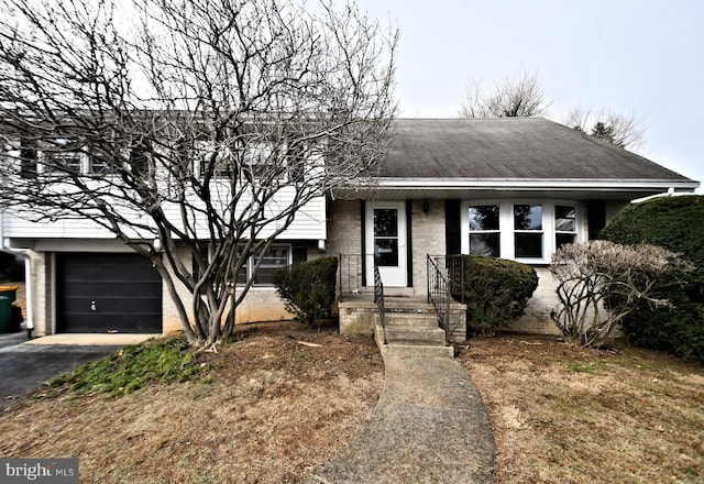 split level home featuring driveway, roof with shingles, and brick siding