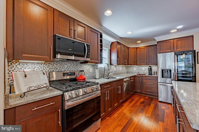 kitchen with crown molding, tasteful backsplash, appliances with stainless steel finishes, a sink, and light stone countertops