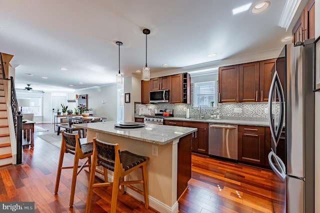 kitchen featuring light stone counters, a kitchen island, appliances with stainless steel finishes, a kitchen bar, and pendant lighting