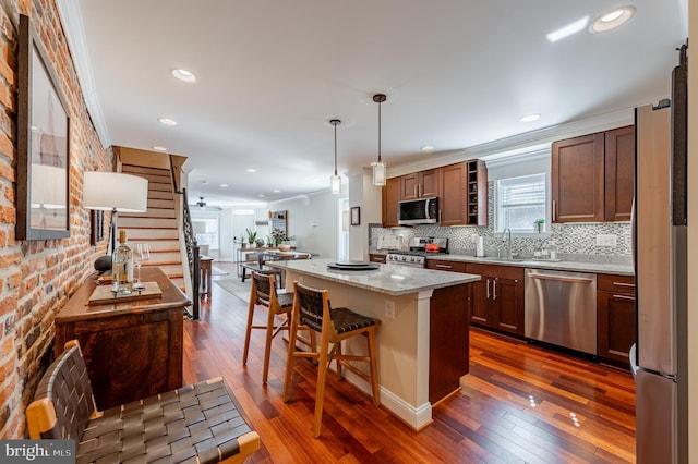 kitchen with a center island, hanging light fixtures, light stone countertops, stainless steel appliances, and crown molding