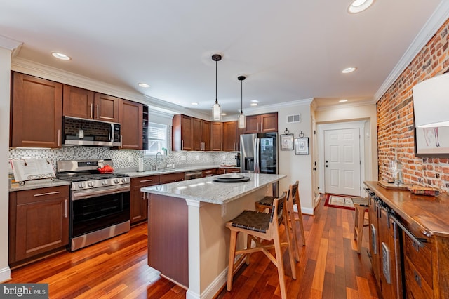 kitchen with a breakfast bar area, appliances with stainless steel finishes, light stone counters, a center island, and pendant lighting