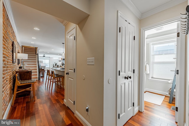 hall with hardwood / wood-style flooring, brick wall, baseboards, and crown molding